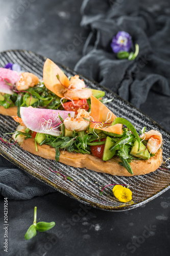 Italian bruschetta with shrimp and salad. Served on a black plate