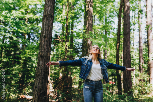 Young blond woman enjoying the nature, outstretched arms while enjoying the fresh air in green forest