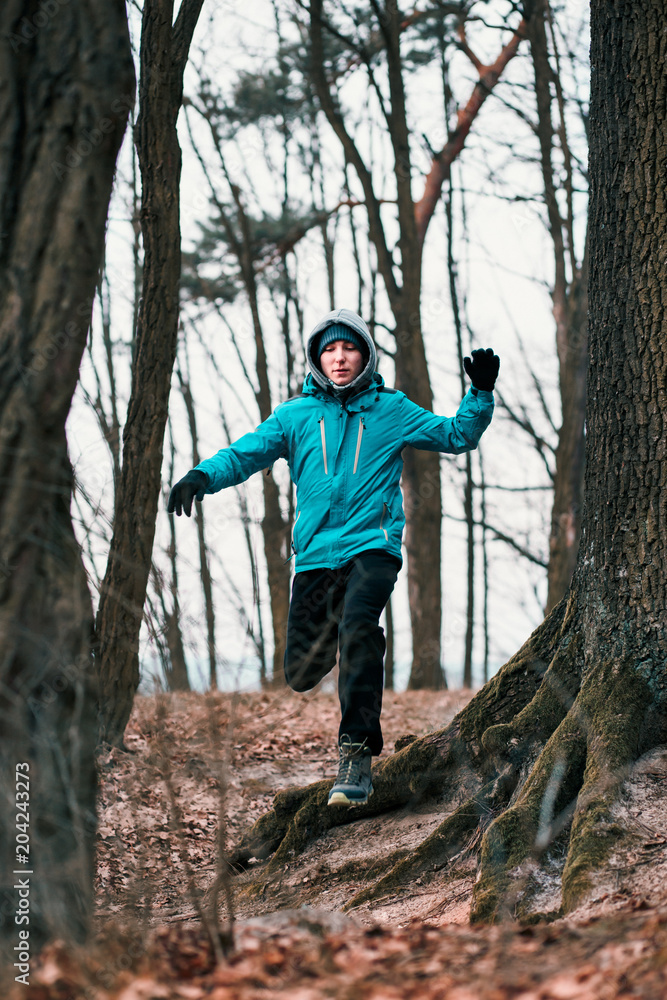 Naklejka premium Young man running outdoors during workout in a forest among leafless trees on cold freeze autumn day