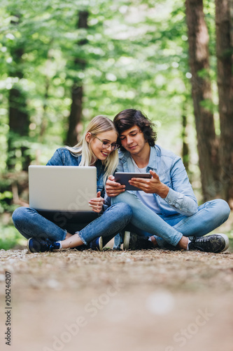 Young couple using laptop and tablet while sitting in forest photo