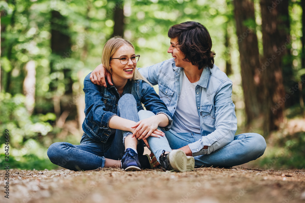 Fototapeta premium Romantic young couple sitting together in forest and enjoying sunny day together