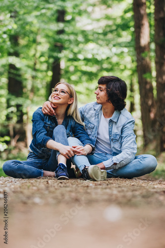 Romantic young couple sitting together in forest and enjoying sunny day together