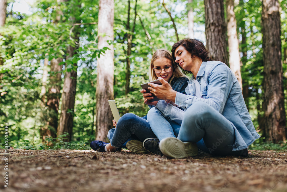 Young couple using laptop and tablet while sitting in forest