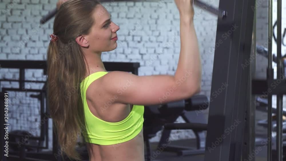 Beautiful young fitness woman working out at the gym. Attractive sportswoman exercising on lat pull gym machine. Female bodybuilder training. Fitness, sports, motivation concept. Beautiful young fitness woman working out at the gym. Attractive sportswoman exercising on lat pull gym machine. Female bodybuilder training. Fitness, sports, motivation concept.