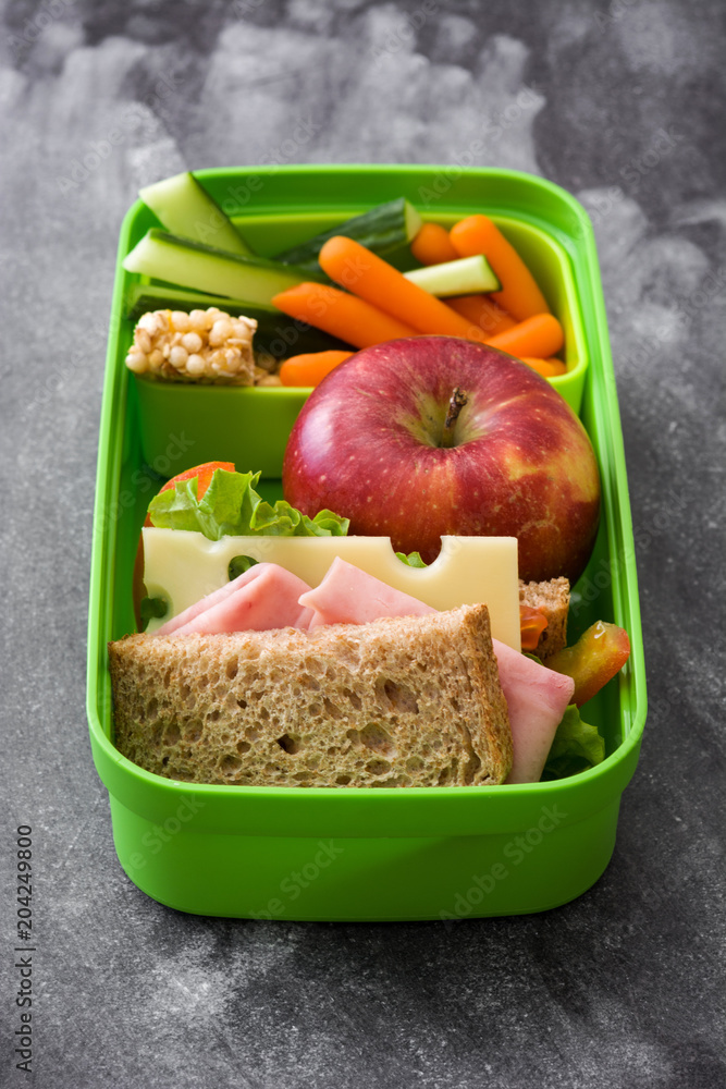 Healthy school lunch box: Sandwich, vegetables ,fruit and juice on black stone Healthy school lunch box: Sandwich, vegetables ,fruit and juice on black stone
