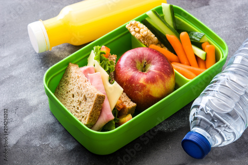 Healthy school lunch box: Sandwich, vegetables ,fruit and juice on black stone