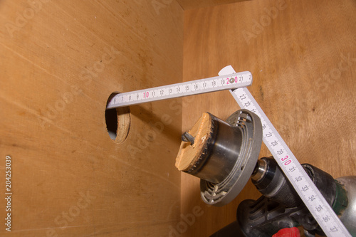 Zollstock Meterstab in Bohrung einer Holzplatte mit Bohrmaschine;
