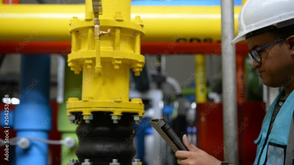 Asian engineer wearing glasses working in the boiler room,maintenance checking technical data of heating system equipment,Thailand people Asian engineer wearing glasses working in the boiler room,maintenance checking technical data of heating system equipment,Thailand people