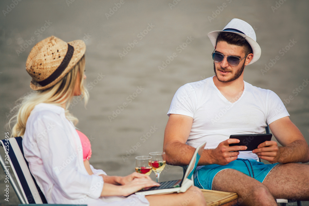 Happy smiling couple surfing the net and enjoy the summer at tropical beach using laptop and digital tablet