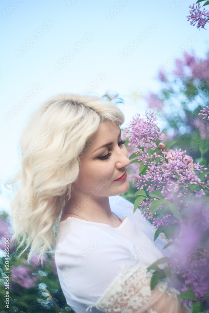 Naklejka premium Beautiful woman in a spring garden with blooming lilacs.