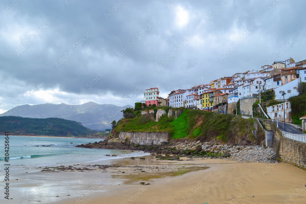 View from the beach of Lastres, Asturias, Spain, of the town, in a cloudy day. Small town in front of the sea over a cliff.