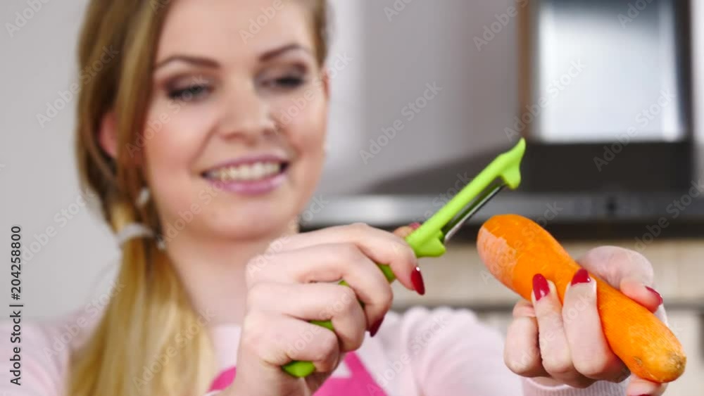 Happy cheerful woman peeling the carrot using kitchen peeler preparing vegetable to cook. Happy cheerful woman peeling the carrot using kitchen peeler preparing vegetable to cook.