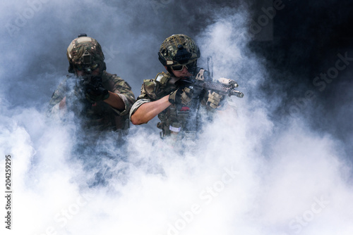 Soldiers or military are gradually walking out of the curtain of smoke with a machine gun in hand.