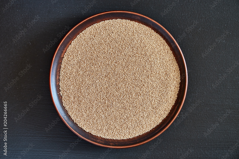 Amaranth seeds on a brown plate on a black background close-up. Amaranth seeds on a brown plate on a black background close-up.
