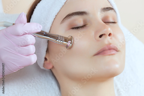 The cosmetologist makes the procedure Microdermabrasion of the facial skin of a beautiful  young woman in a beauty salon.Cosmetology and professional skin care.