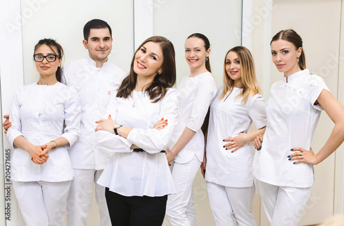 Cheerful group of young dentists and their assistants standing in the dental office and looking at camera and friendly smiling at white background of medical room.