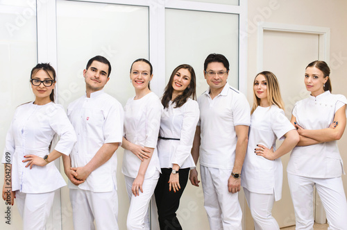Cheerful group of young dentists and their assistants standing in the dental office and looking at camera and friendly smiling at white background of medical room.