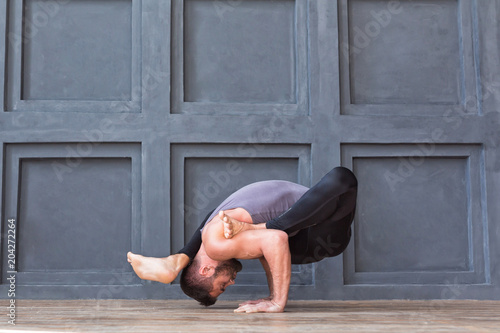 Man doing yoga exercises and practicing handstand balance pose on grey urban background.