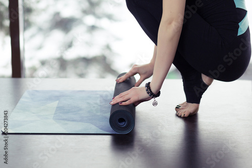 Young yoga Woman rolling her violet mat after a yoga class on wooden floor near a window, close up