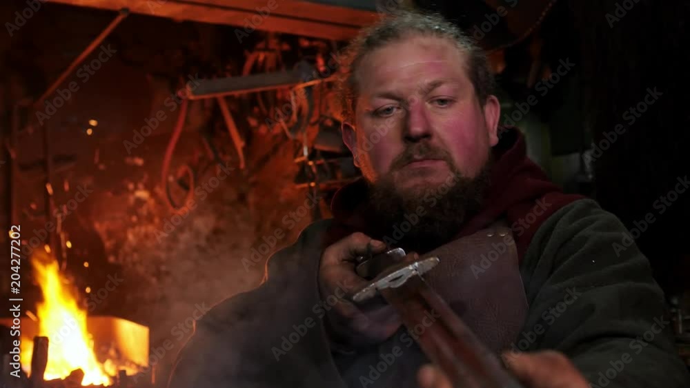 The medieval blacksmith taken sword to examine metal of sword The medieval blacksmith taken sword to examine metal of sword