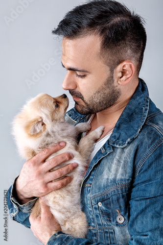 man in denim jacket holds pomeranian dog.