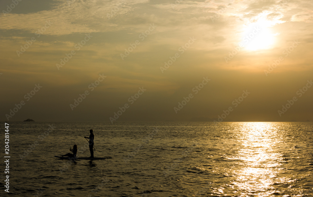 Silhouette of a couple on paddle board on the open sea at sunset in the island of Koh Pha Ngan, Thailand