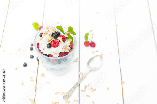 Healthy breakfast: layered dessert yogurt parfait with fresh raspberries and black currant on wooden table over garden photo