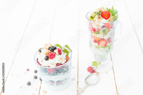 Layered dessert with raspberry, strawberry, black currant and kiwi, cream and biscuits in glasses photo