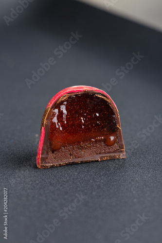 Handmade candy with with chocolate ganache and red confiture on black background. Exclusive handcrafted bonbon