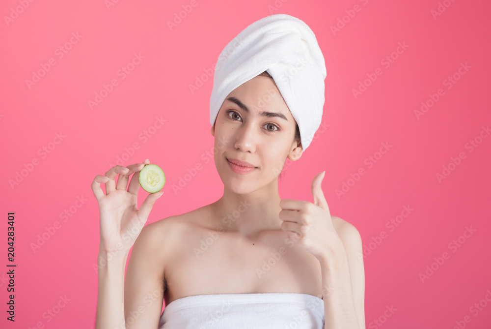 beautiful asia woman with towel on head with perfect clean skin smiling holding cucumber slices over pink background. Beauty cosmetology and spa. beautiful asia woman with towel on head with perfect clean skin smiling holding cucumber slices over pink background. Beauty cosmetology and spa.