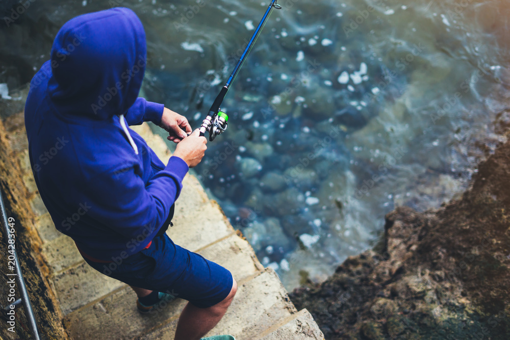 young man holds a fishing rod and catches fish in the nature on a sea background, hipster fisherman spends vacation on the blue ocean, active travel hobby fishing, rural outdoor sport tourism young man holds a fishing rod and catches fish in the nature on a sea background, hipster fisherman spends vacation on the blue ocean, active travel hobby fishing, rural outdoor sport tourism