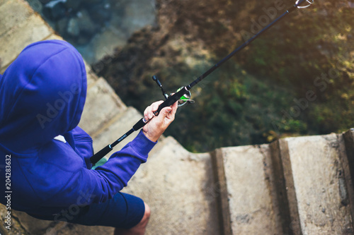 young man holds a fishing rod and catches fish in the nature on a sea background, hipster fisherman spends vacation on the blue ocean, active travel hobby fishing, rural outdoor sport tourism © A_B_C