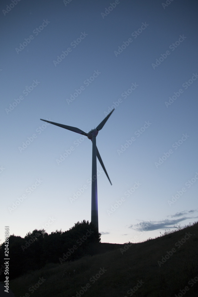 Single windmill in the nature during the blue hour in the morning with silhouettes of bushes Single windmill in the nature during the blue hour in the morning with silhouettes of bushes