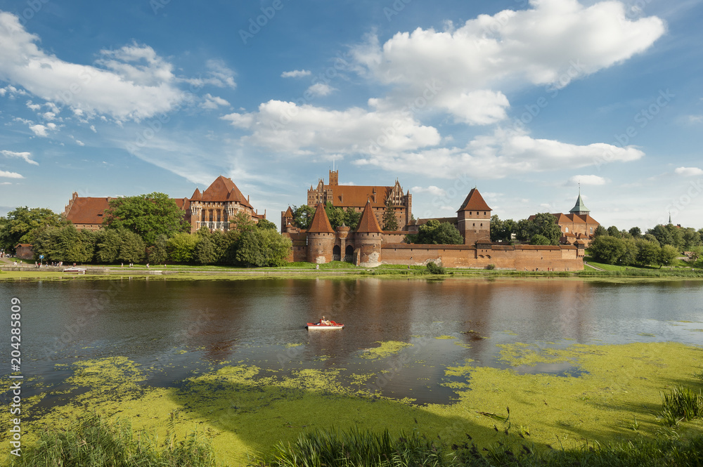 Marlbork castle in northern Poland/largest castle in the world built by the Teutonic knights in the thirteenth century seen across a pond where tourist ride a hydro bicycle.
