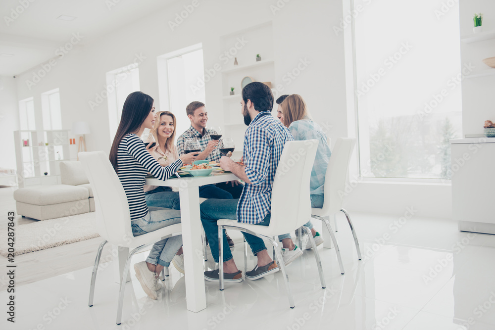 Full size portrait of cheerful, stylish, best, attractive friends sitting at the table in modern dinning room eating having wineglasses in hands enjoying time together celebrating holiday
