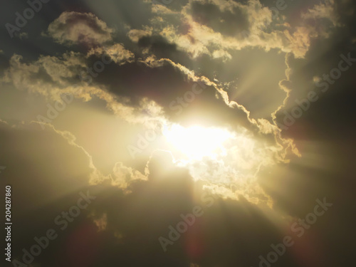 Glowing sun hide and seek behind in clods on a cloudy day, camera facing directly to at sun day time photo with sun rays beam