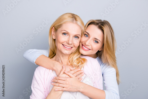 Portrait of stylish cute attractive charming mother and daughter, family with one single parent, warm hugs, looking at camera isolated on grey background