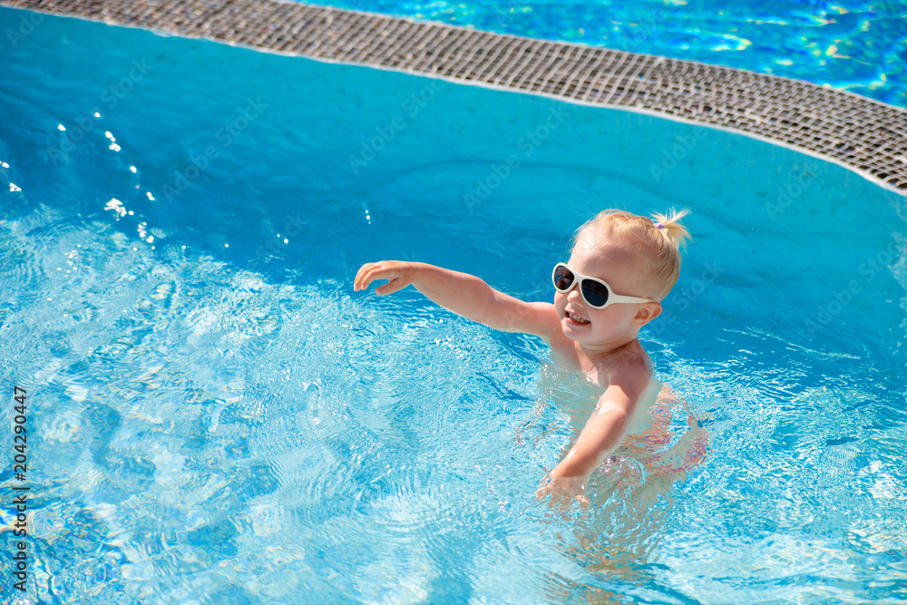 The child splashes in the pool with clear water in the summer illuminated by the sun. Top view. Copy space.