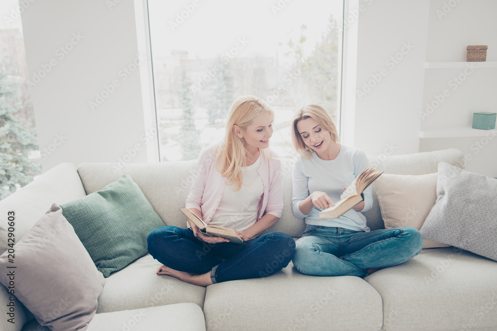 Cute educated girl showing page interesting moment to her mother with index finger having best-seller in hands, books lovers, hobby concept, comfortable cozy atmosphere, free-time
