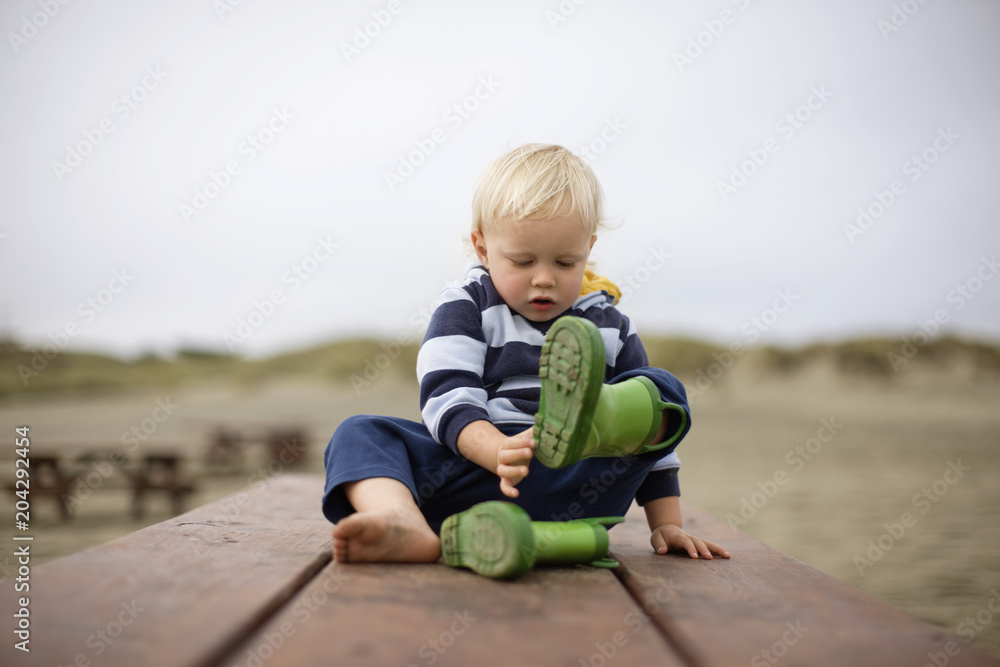 Boy removing his boots while sitting on bench outdoors Boy removing his boots while sitting on bench outdoors