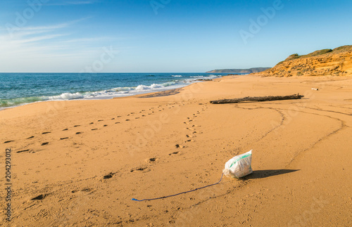 Footprints and garbage on a beach in a sunny day