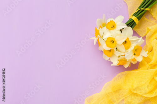 Fototapeta Naklejka Na Ścianę i Meble -  Daffodil bouquet with yellow textile decoration on violet pastel background with copy space.
