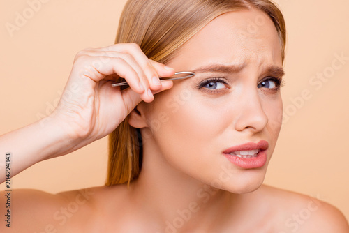 Wall Mural Patient, pretty, nude, natural model looking at camera plucking eyebrows with tw