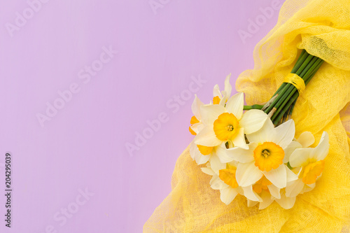 Fototapeta Naklejka Na Ścianę i Meble -  Daffodil bouquet with yellow textile decoration on violet pastel background with copy space.