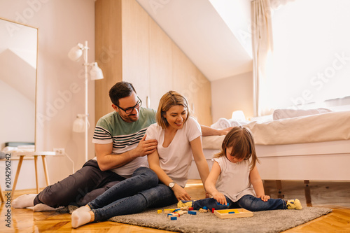 Young parents playing with wooden toy with daughter on bedroom floor