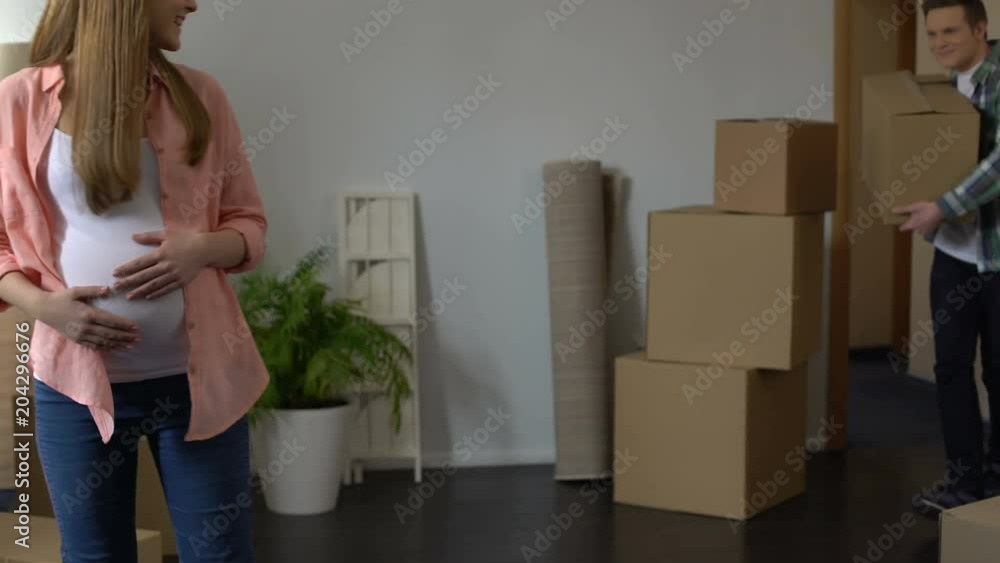 Pregnant girl viewing new apartment while her husband carrying boxes, crediting Pregnant girl viewing new apartment while her husband carrying boxes, crediting