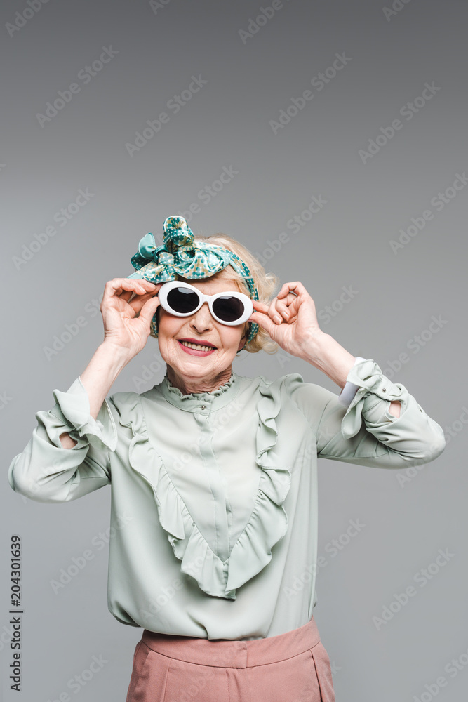 smiling senior woman in stylish headband and sunglasses isolated on grey