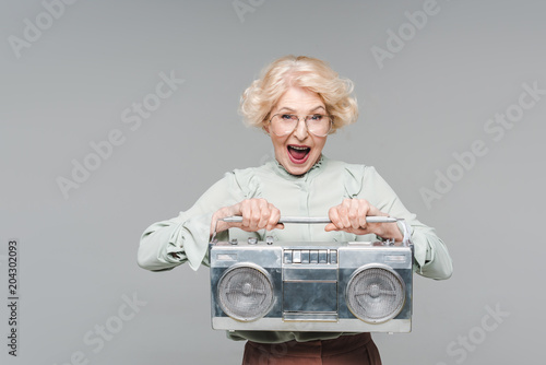 shouting senior woman with boombox isolated on grey photo