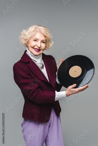 beautiful senior woman holding vinyl disc isolated on grey