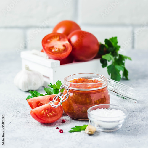 Homemade roasted tomato sauce in glass jar, garlic, pepper, salt on concrete background. Selective focus, space for text.